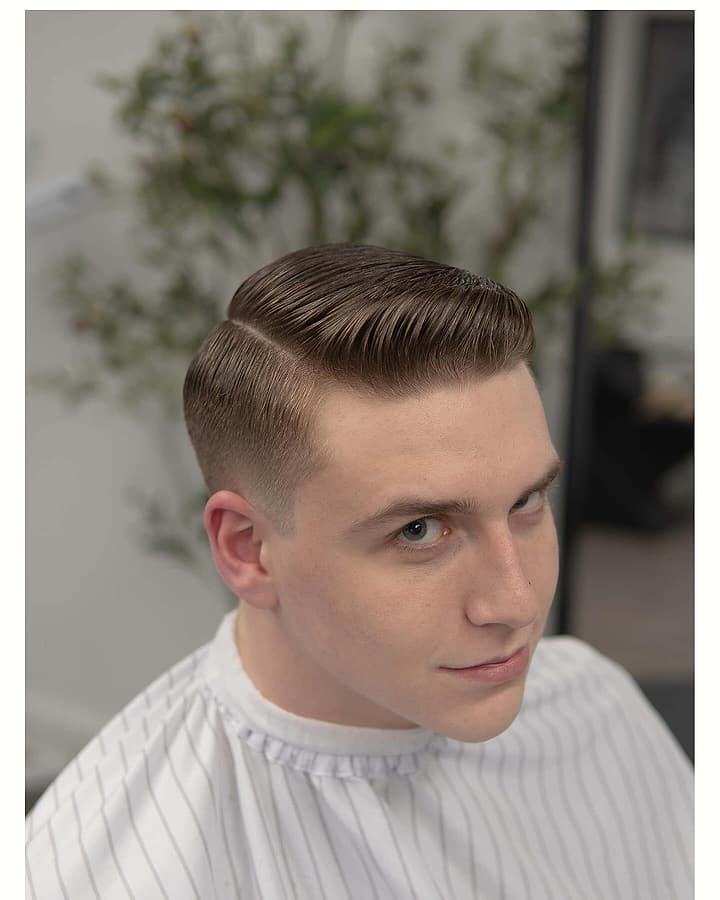 Client seated in the barber chair with a classic side part and a taper fade